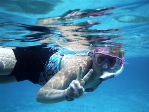 mujer rubia saludando a la camara mientras bucea en Cozumel