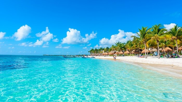 Paisaje de la playa con agua turquesa cristalina con ala rena blanca, palmeras y una pareja de turistas a lo lejos